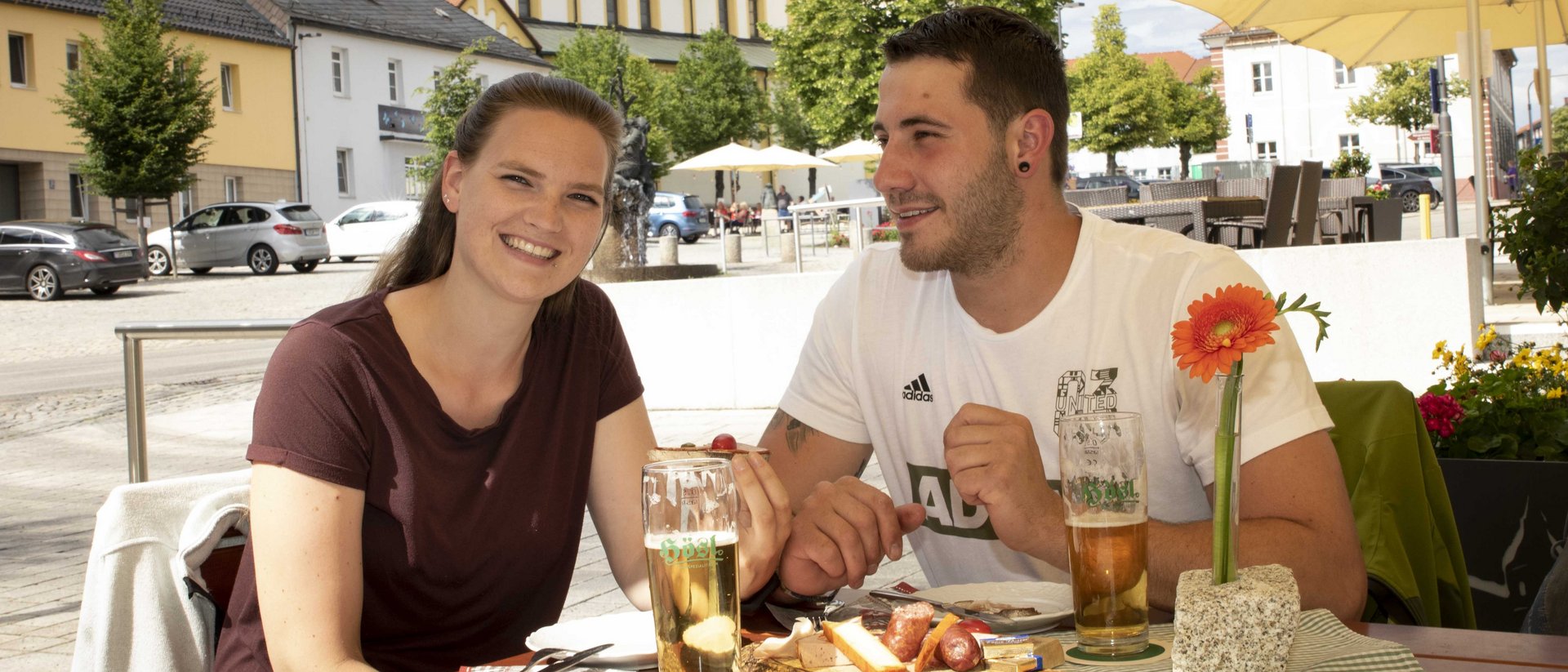 Ein Mann und eine Frau sitzen am Marktplatz Mitterteich. Auf dem Tisch vor ihnen befinden sich zwei Gläser Zoigl-Bier.
