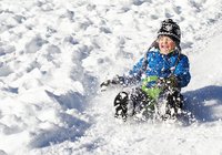 Bild: Ein kleines Kind, welches im Winter einen Berg hinunter rodelt 