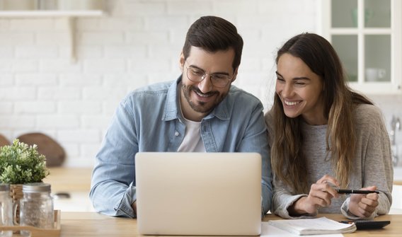 Bild: Eine Frau und ein Mann schauen fröhlich in den Laptop.
