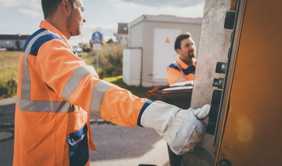 Bild: Zwei Müllmänner, die eine Mülltonne in ein Müllfahrzeug entleeren. 